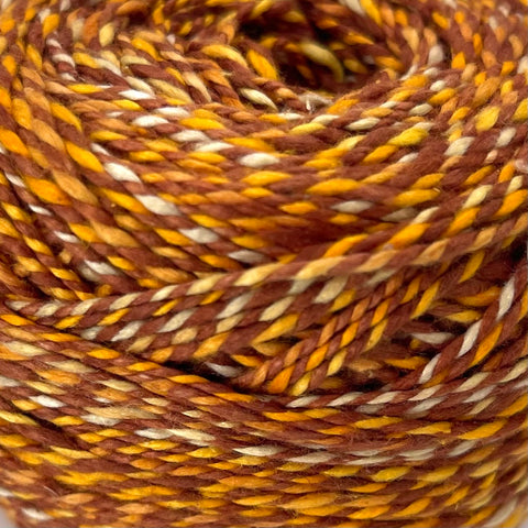 A closeup of a skein of twist sport weight yarn in shades of caramel brown, white, and warm yellow.