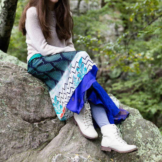 Model is sitting on a rock wearing a blue maxi length sari wrap skirt in our women's size. 