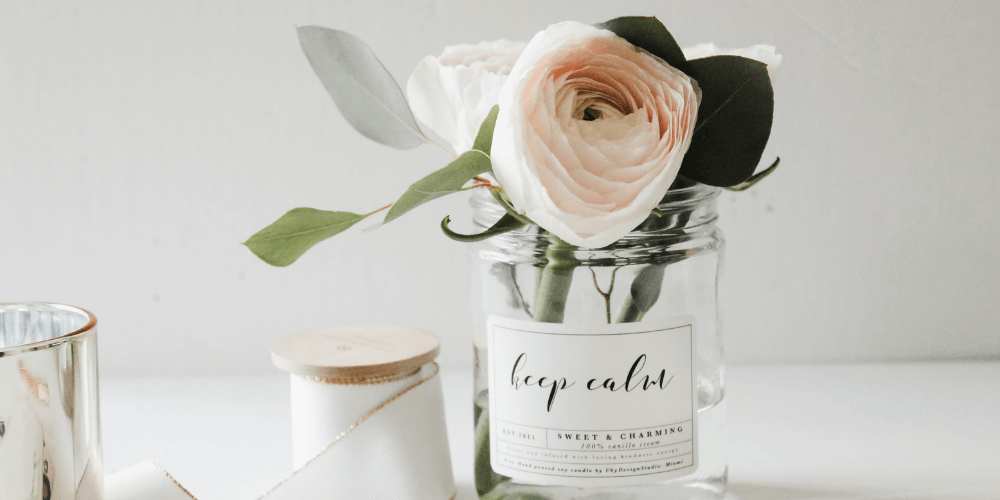 White candle next to a glass jar with pastel pink roses