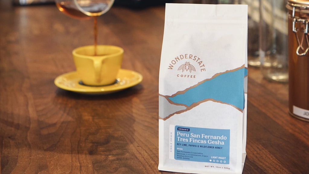 A bag of Peru Gesha sits next to a yellow coffee cup