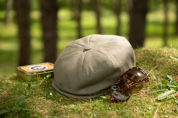 A khaki linen cap sitting on the grass with a pair of sunglasses