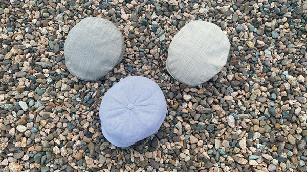 Drei Leinenmützen sitzend auf bunten Steinen.