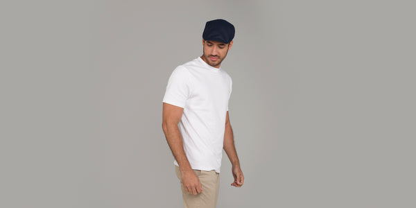 A man wearing a white t-shirt and a dark coloured linen flat cap