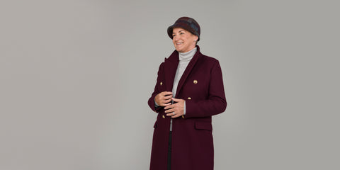 Eine Frau trägt einen beerenroten Mantel und einen Tweedhut im Stil der 1920er Jahre