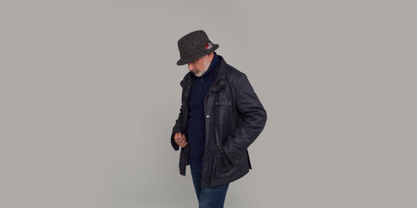 Man wearing a dark coat and dark grey tweed hat.