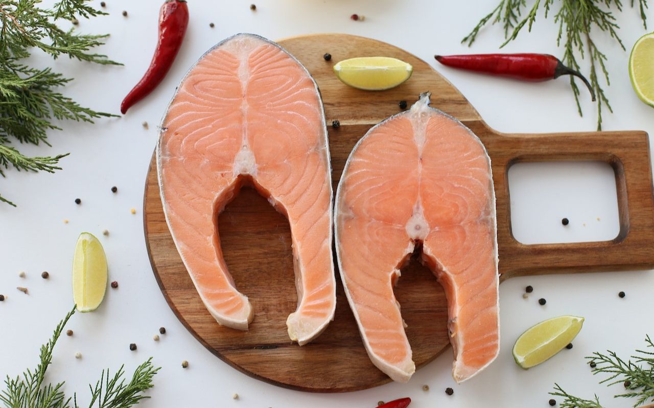 Salmon on a wood board with peppers and lemon around it