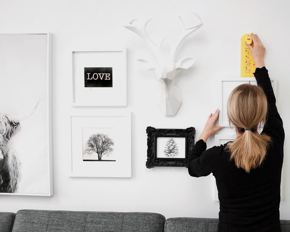 Person hanging a gallery wall with various decor items using Hang & Level, the picture hanging tool that marks exactly where to put the nail.