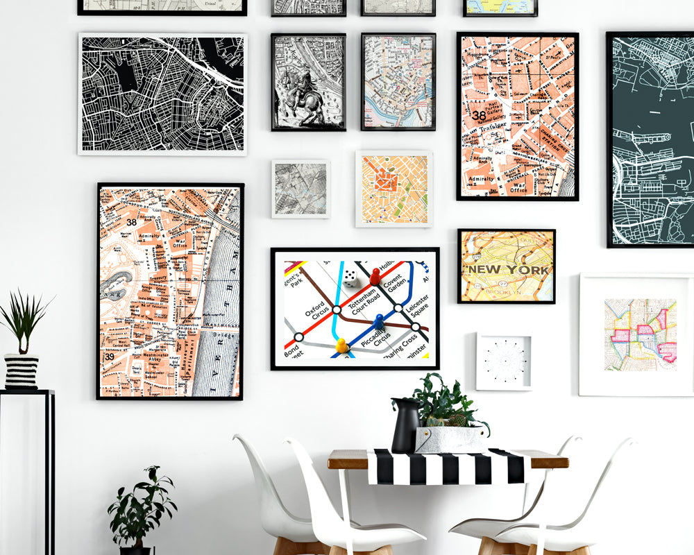 Gallery wall of 16 different sized frames all with a theme of maps of New York City, styled with a table and chairs.