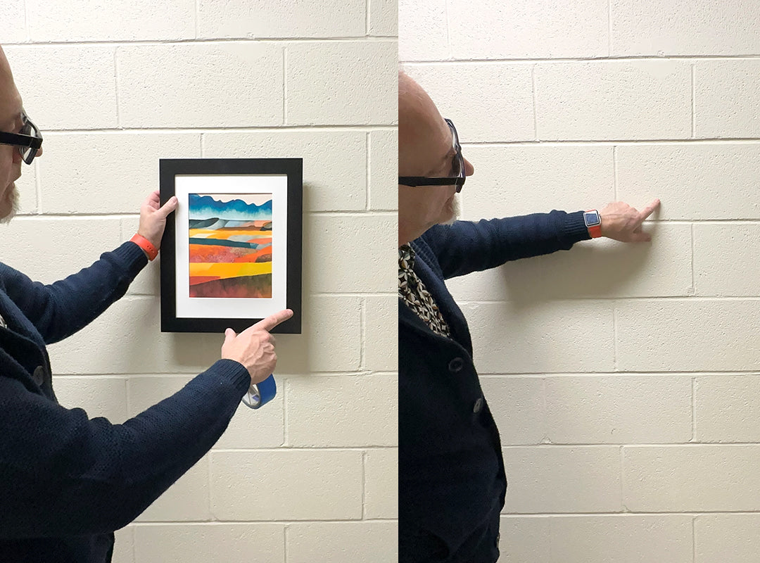 Two pictures together: one showing a person holding a picture where they want it to hang on a hard wall surface so they can see approximately where the fastener will go. The second image shows the person pointing to the area on the wall where the fastener will go.