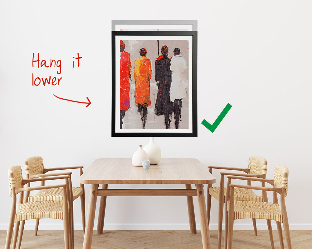 Picture hung above a table and chairs with it hung in two different spots - start by hanging it lower, correct and then if need to hang it higher then the nail hole of the first image is hidden.