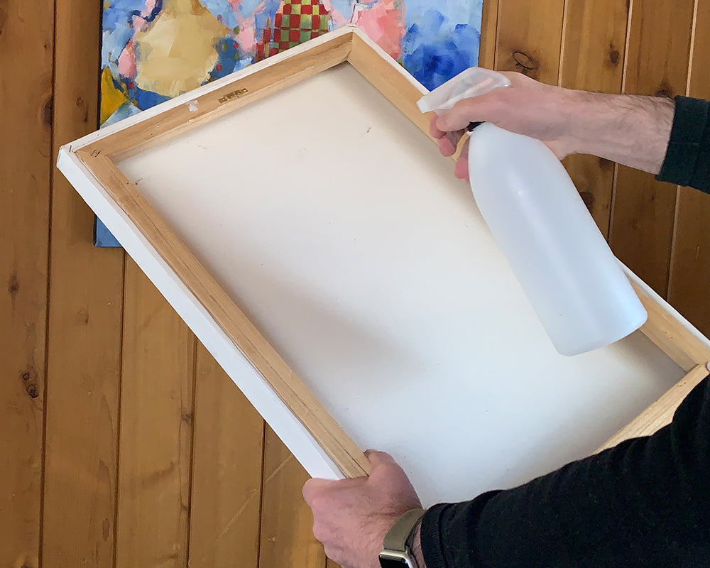 Image showing how to use a spray bottle to spritz water onto the back of a canvas art piece in order to tighten sagging canvas