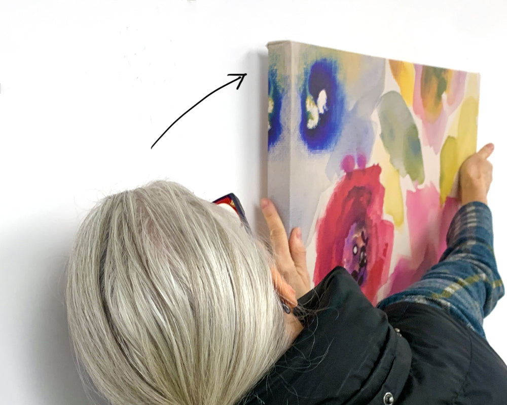 A person looking at the side of the canvas art to align the pin from CanvasHangers into the original hole on one side