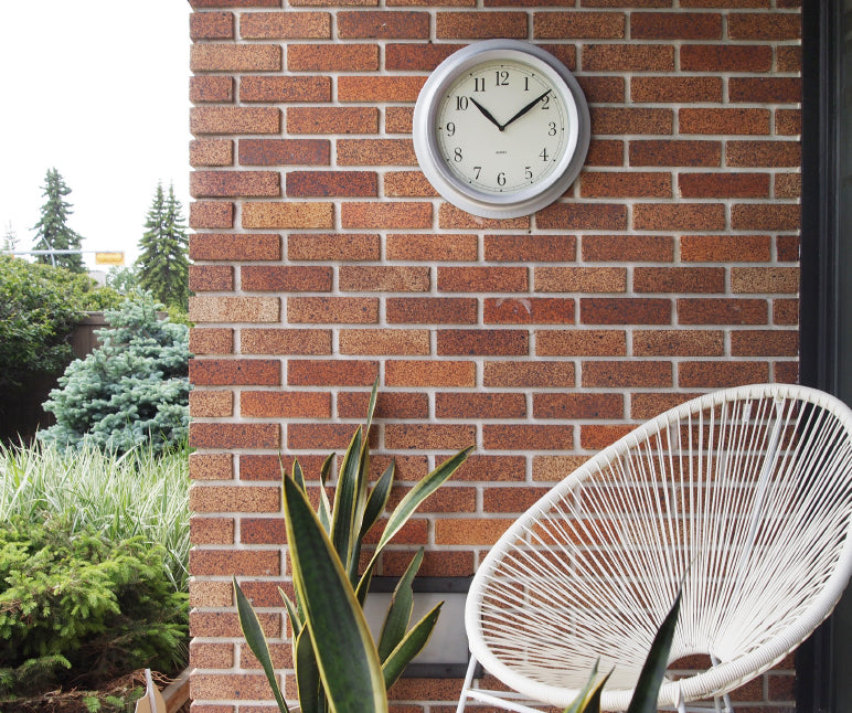 Image using showing a clock hung outdoors on a brick wall that was hung with the reusable and damage-free DécoBrick™ hanger