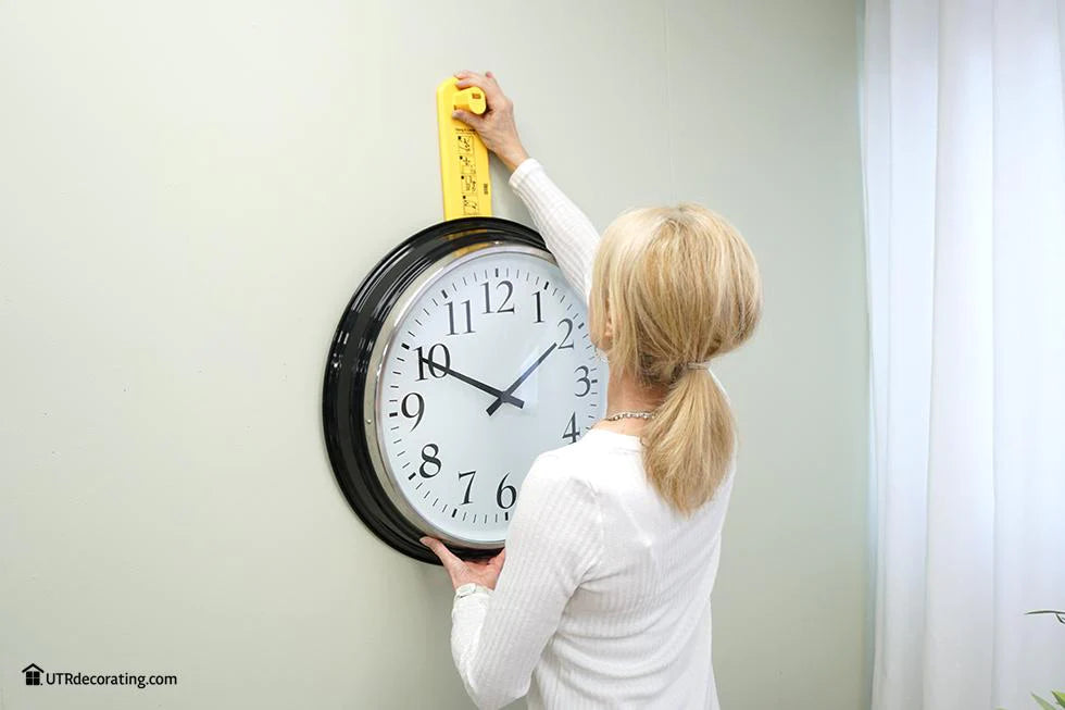 Image of a person using Hang & Level™ the picture hanging tool that marks exactly where the nail goes, to hang a large Ikea clock.