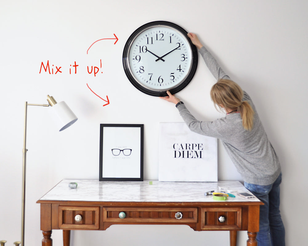 image showing a person adding a clock to a decorating vignette with the words 'mix it up' meaning you can combine a clock and pictures