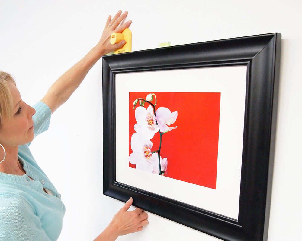 A person hanging the second side of a picture with Hang & Level™, the picture hanging tool that marks exactly where to put the nail. The first side is already hung using Hang & Level.