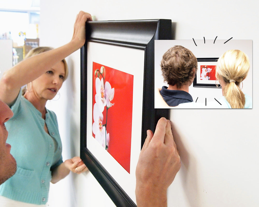 two people hanging the picture installed with two keyhole hangers after installing the fasteners using Hang & Level™, the picture hanging tool that marks exactly where to put the nail.