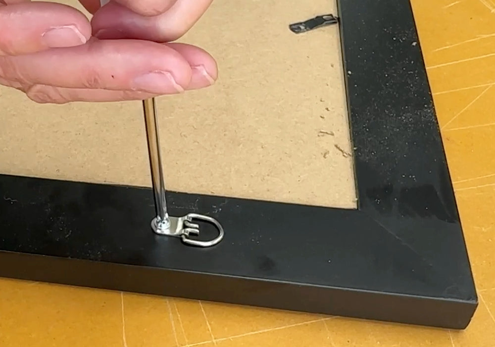 Pictue showing a person installing the screw for the d-ring on the back of a picture frame using a screwdriver