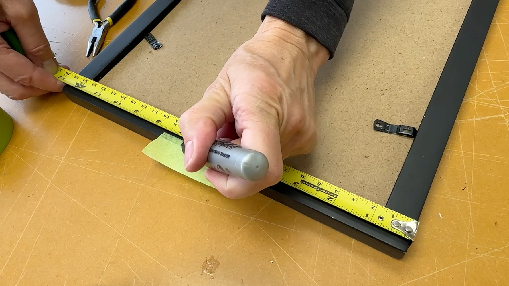 Person marking the centerpoint on a piece of Painter's tape on the top of the frame profile, using a tape measurer and marking pen.