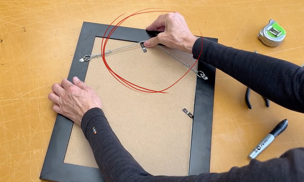 Person testing the installed picture wire on the back of the frame by pulling it upward