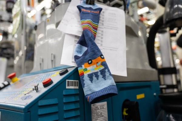 Children's sock hanging off a knitting machine with instructions next to it