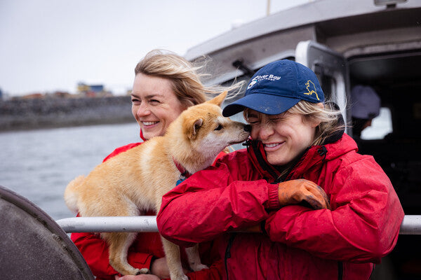 Emma and Claire on the boat, their dog licking their faces