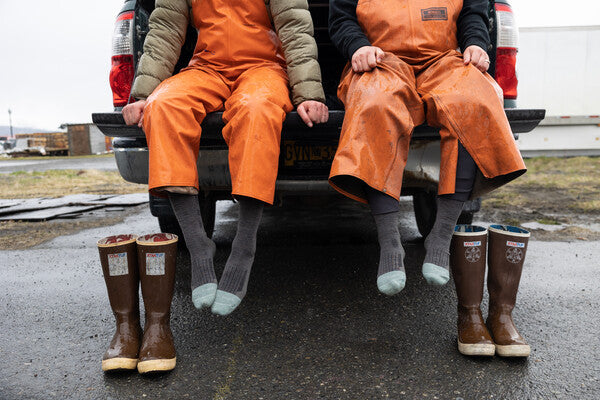 Two fisherman putting on their rubber boots over their darn tough work socks