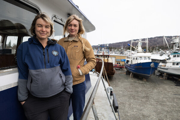 Emma and Claire standing on their boat with other fishing vessel's visible behind them