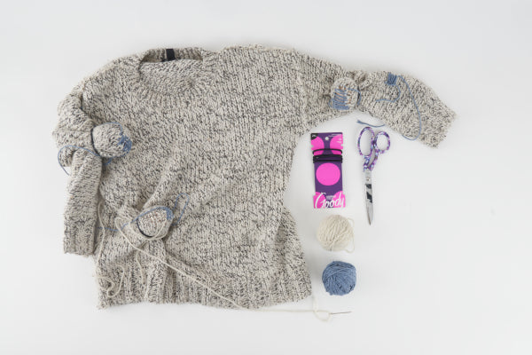 A sweater waiting to be darned with scissors, thread, and darning mushrooms at hand