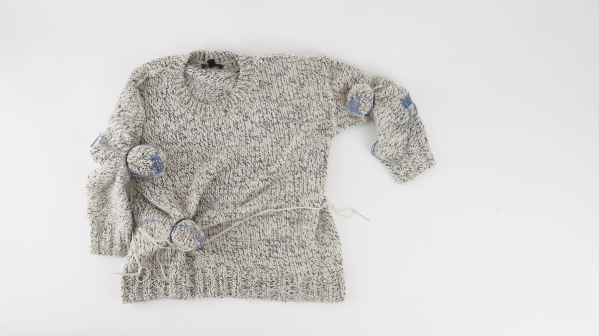 A knit sweater with several holes getting darned
