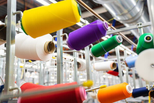 Super bright yellow, orange, and purple yarns hanging on knitting machines at the Mill