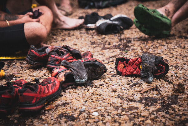 A pile of dirty trail running shoes and wool socks covered in mud