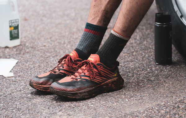 A pair of feet in trail runners and mismatched darn tough socks