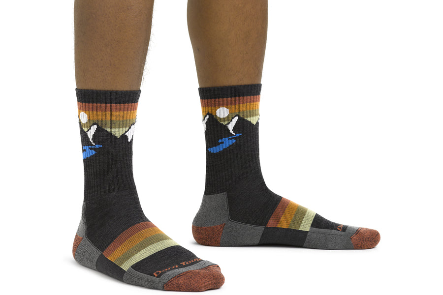 Feet wearing the Sunset Ridge hiking socks, featuring mountains, a river, and dramatic sunset