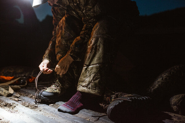 Hunter pulling on hunting boots over darn tough hunting socks at night in truck bed
