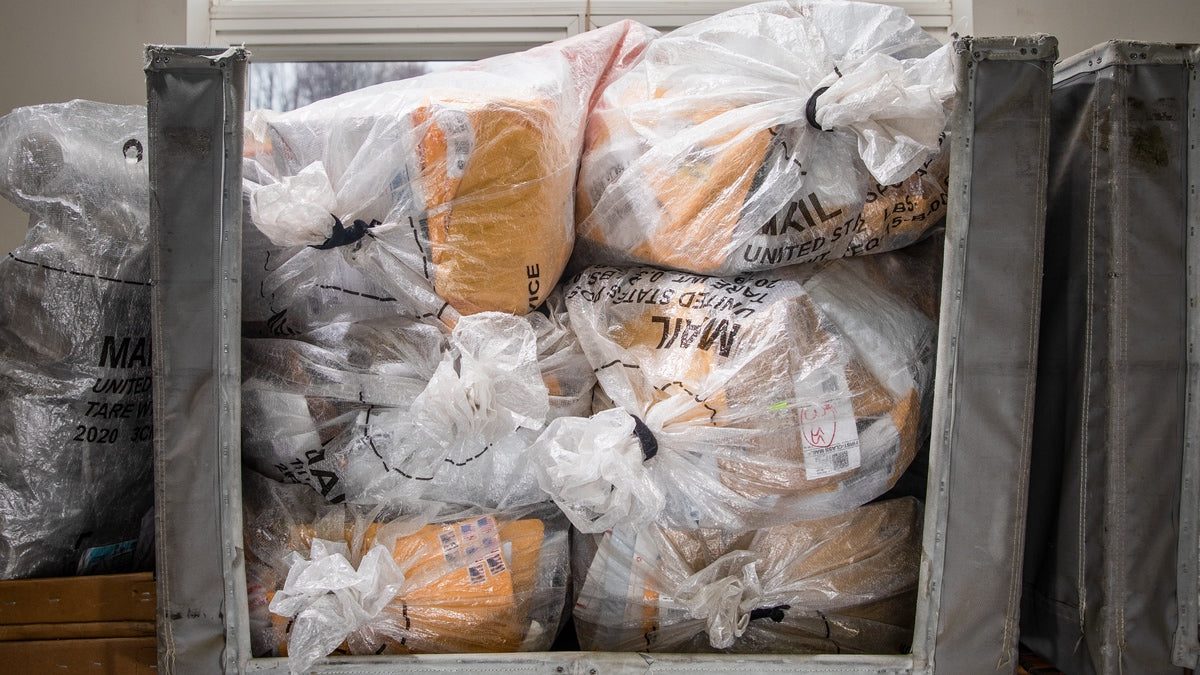 A rolling cart filled to the brim with packages from the post office for Darn Tough