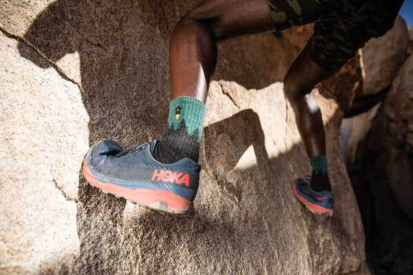 Close up of a foot wearing the number 2 rocket ship outhouse socks and climbing a rock slab