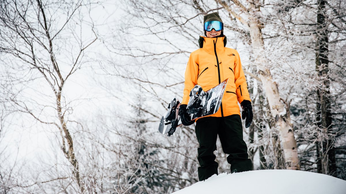 Jake Blauvelt, professional snowboarder, standing in the snow holding his snowboard