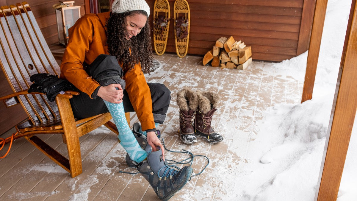 Woman on back porch pulling on boots over snow socks, getting ready for the new year