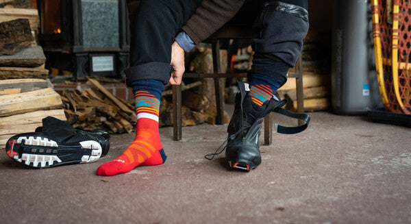 Cross country skier pulling on boots over orange wool nordic socks