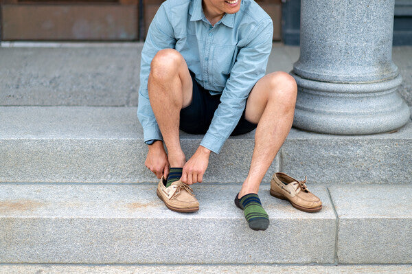 Man pulling on loafers over no show merino wool socks on a sunny day