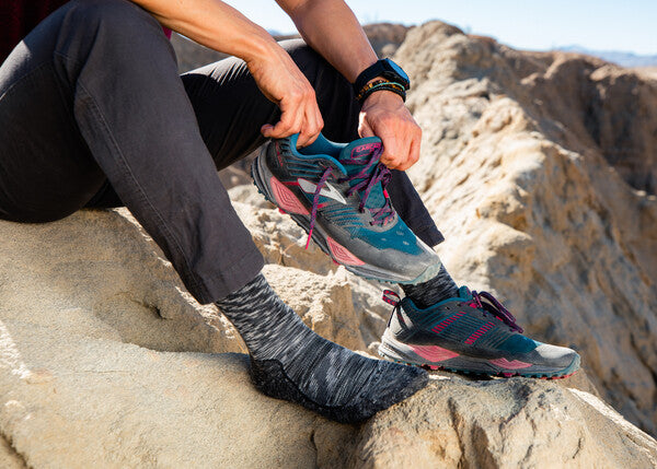 Hiker seated on rock putting hiking shoes on over space gray lightweight wool socks