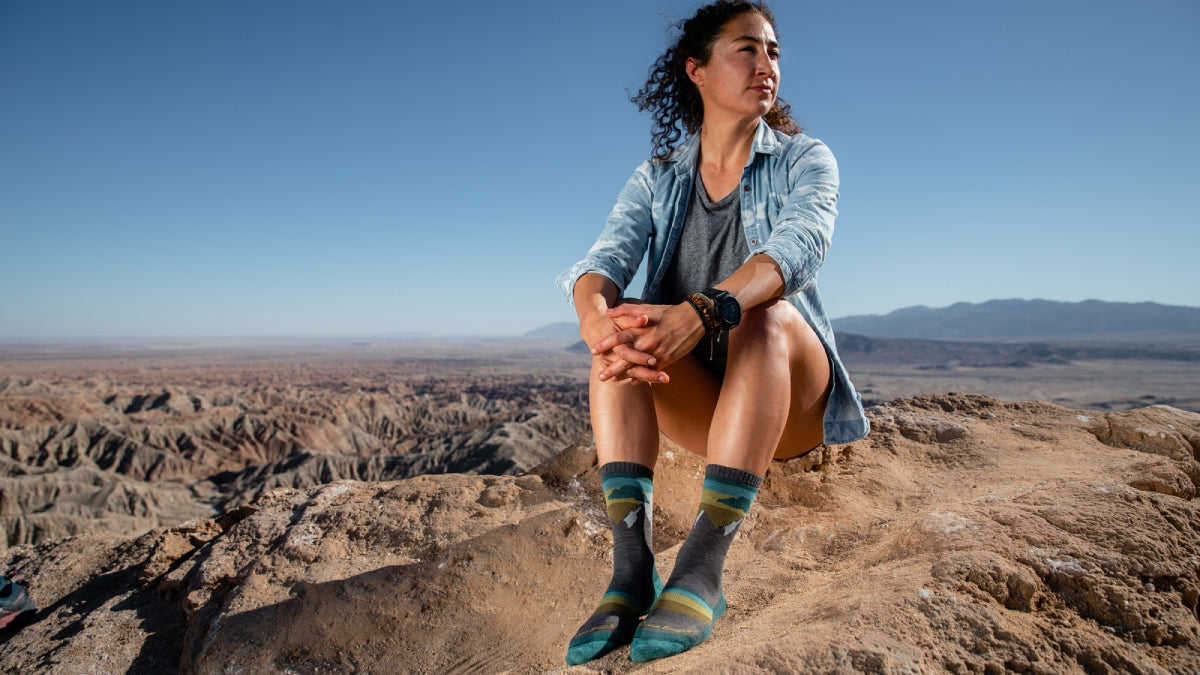 Lady hiker seated on summit wearing Darn Tough women's hiking socks