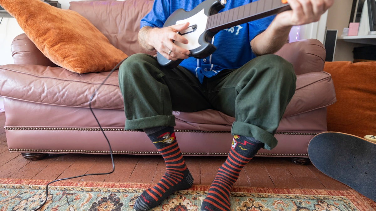 Person seated on couch playing Guitar Hero while wearing the Animal Haus socks