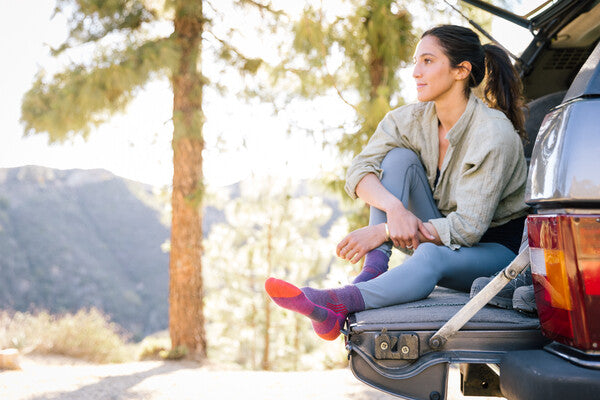 A female hiker seated on her car trunk wearing the hiker quarter socks in purple
