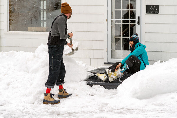 Two people shoveling out the driveway on a snowy day wearing darn tough socks