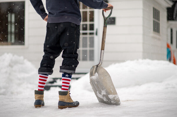 Person with shovel surveying the snow they just finished moving, wearing the Captain Stripe American flag socks