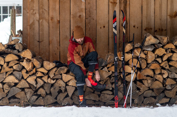 Nordic skier seated on woodpile putting on boots to head out