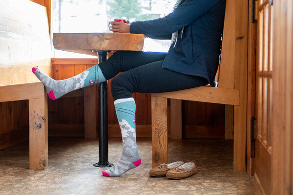 Person seated in lodge wearing socks with a mountain design featuring a hidden yeti