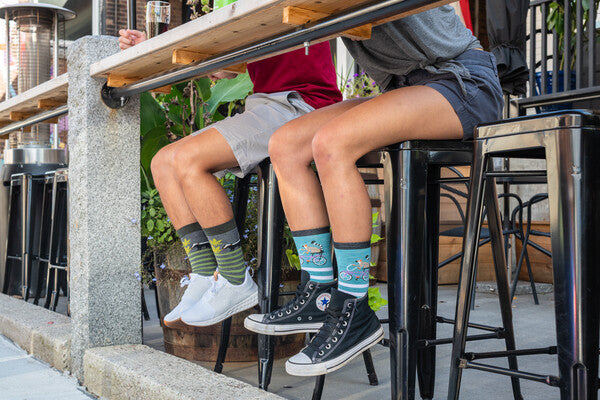 People seated at outdoor restaurant, both wearing animal socks from darn tough
